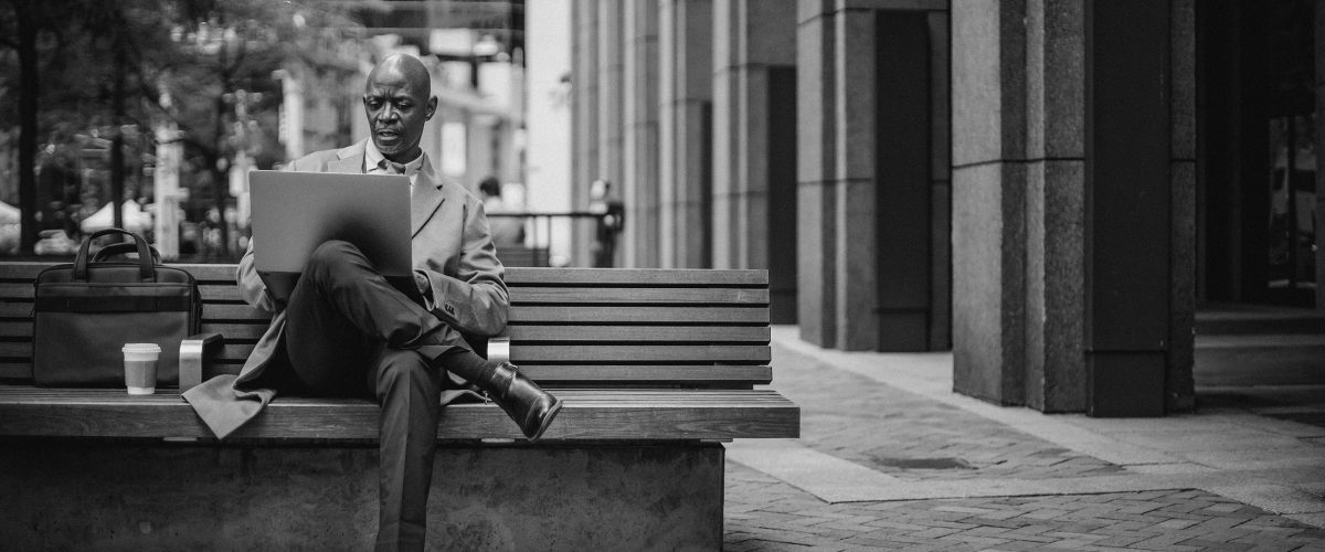 Executive at sitting on bench outside office building looking at laptop